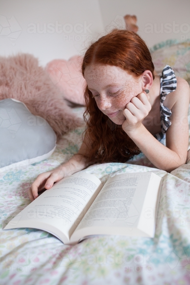 Girl reading a book on a bed - Australian Stock Image