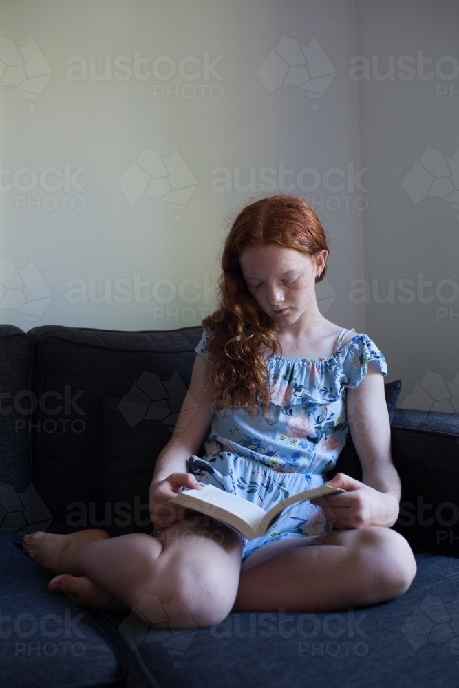 Girl reading a book on a lounge - Australian Stock Image