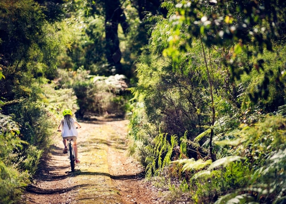 Girl riding a bike down a dirt road surrounded by dense bush - Australian Stock Image