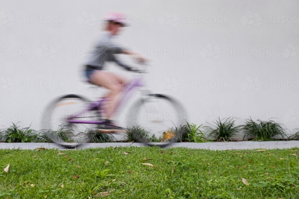 Girl riding bike along urban street with motion blur. - Australian Stock Image