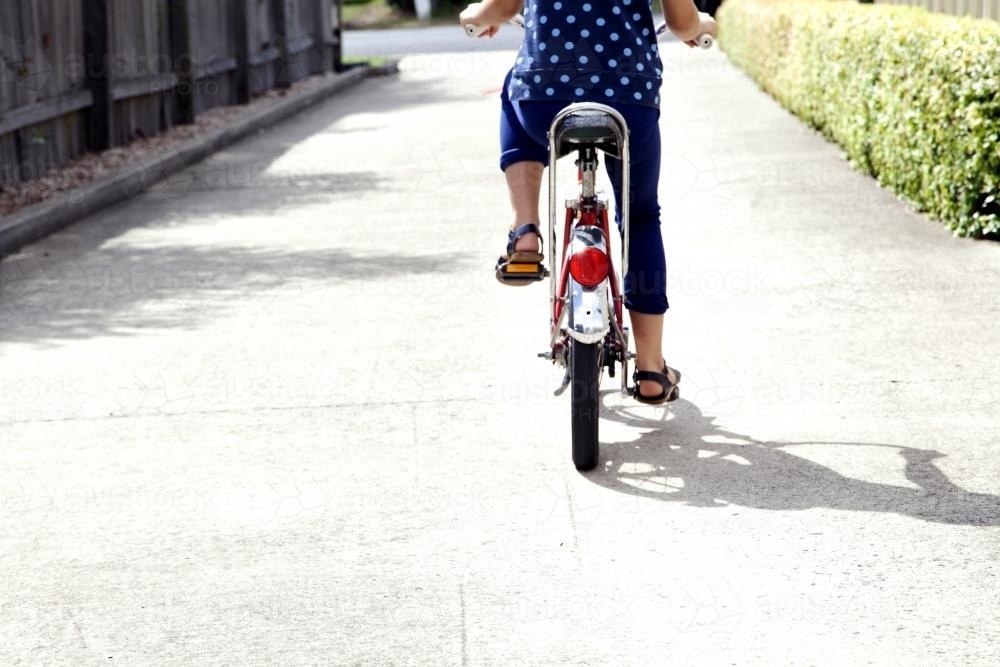 Girl riding bike down driveway from behind - Australian Stock Image