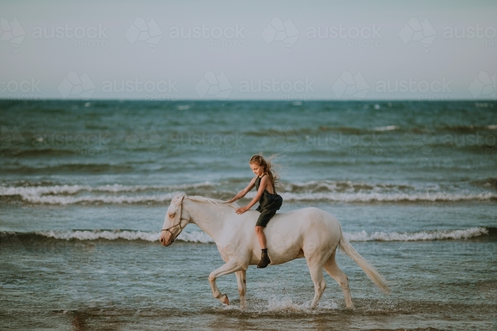 Girl riding horse in ocean waves - Australian Stock Image