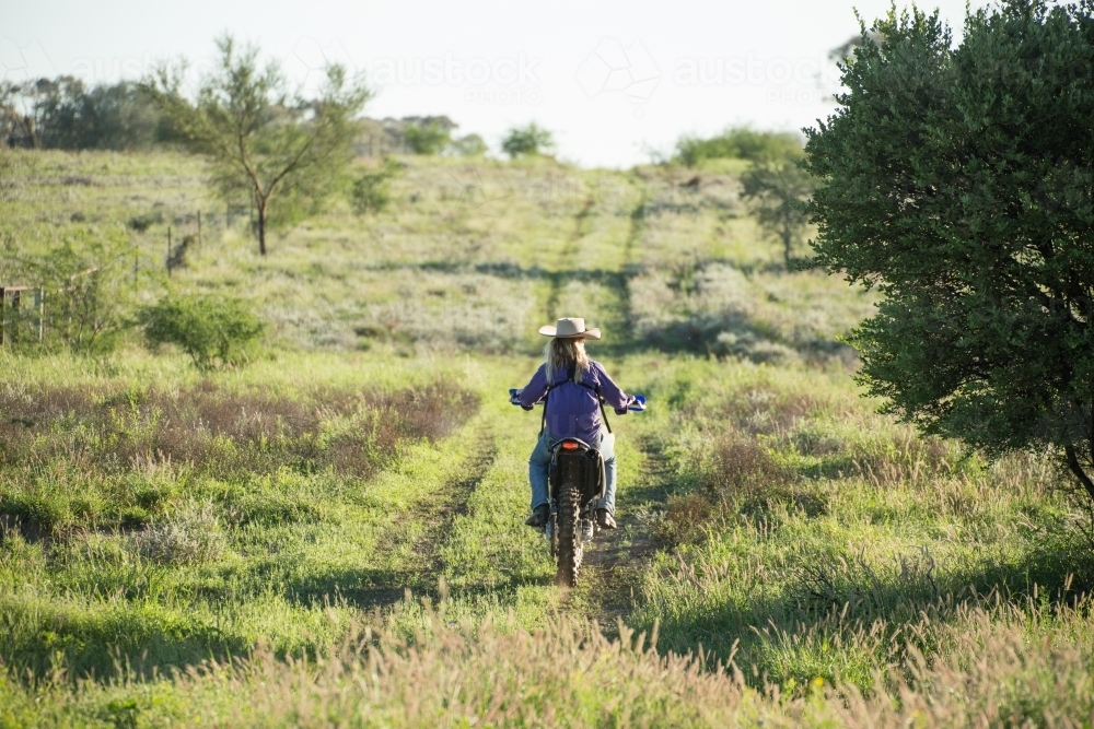 Girl riding motorcycle on grassy farm track - Australian Stock Image