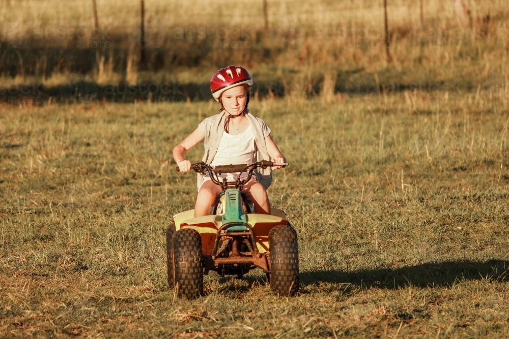 Girl riding quad bike wearing helmet on farm - Australian Stock Image