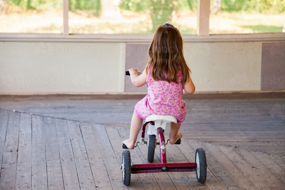 Girl riding tricycle on veranda at homestead - Australian Stock Image