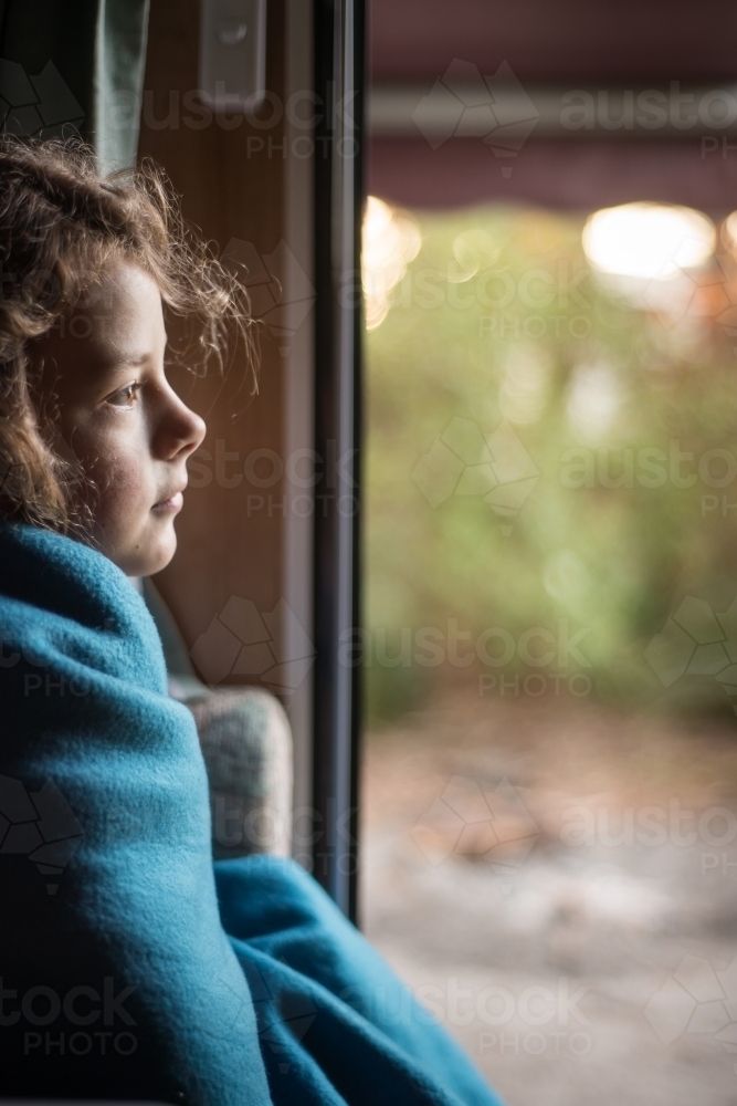 Girl rugged up inside caravan door looking out to bush - Australian Stock Image