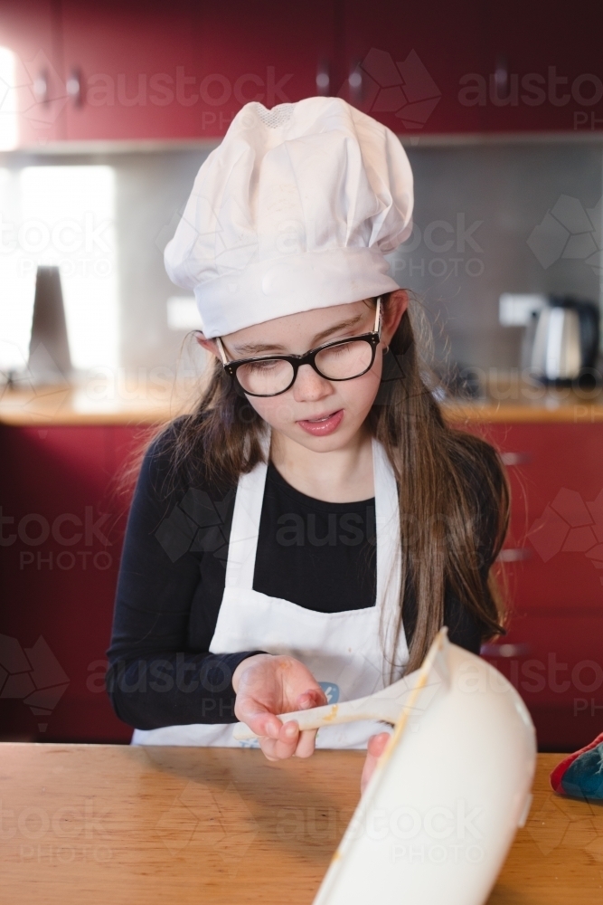 Girl scraping bowl cooking cake - Australian Stock Image