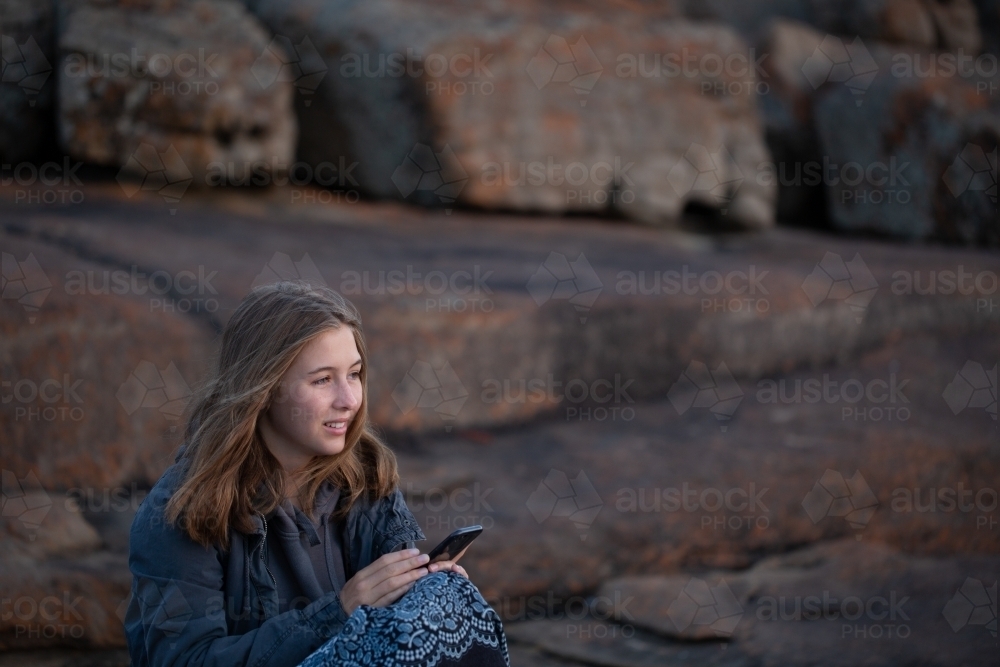 Girl sitting alone outdoors with iPhone - Australian Stock Image