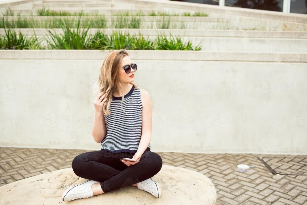 Girl sitting cross-legged wearing sunglasses - Australian Stock Image