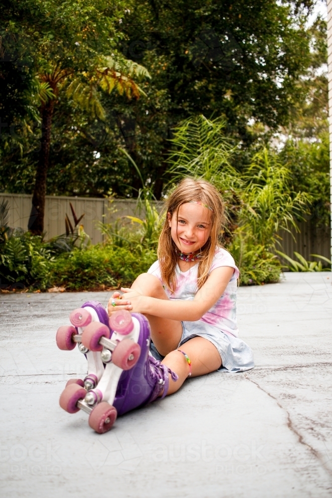 Girl sitting down on the ground with her roller skates on - Australian Stock Image