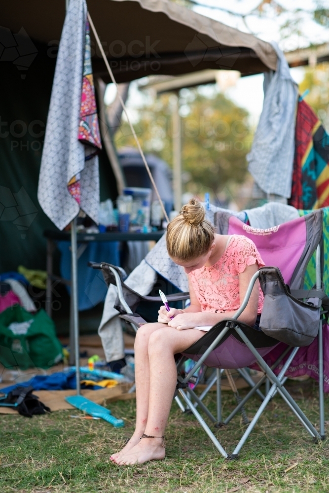 Girl sitting in camping chair writing her journal - Australian Stock Image