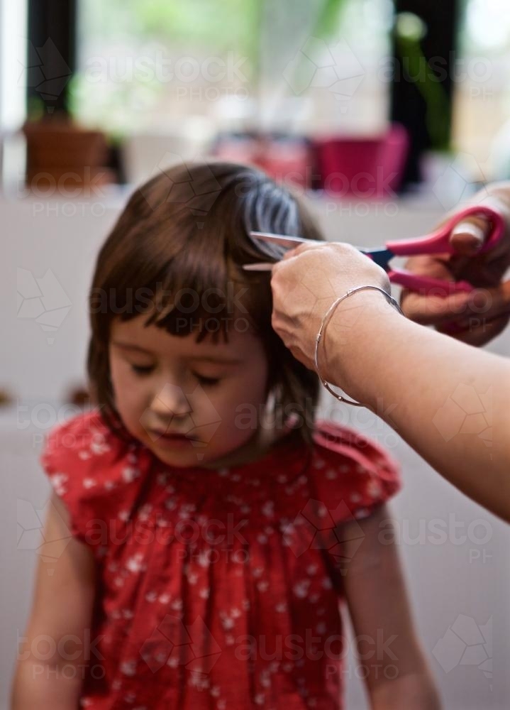 Girl sitting on a chair having her hair cut by her mother - Australian Stock Image