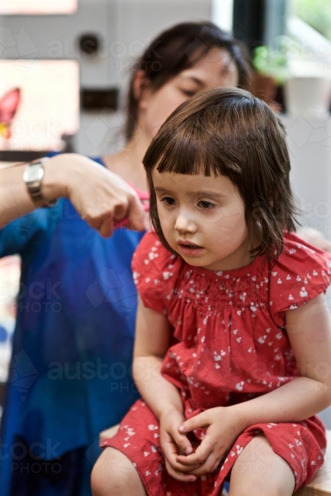 Girl sitting on a chair having her hair cut by her mother - Australian Stock Image
