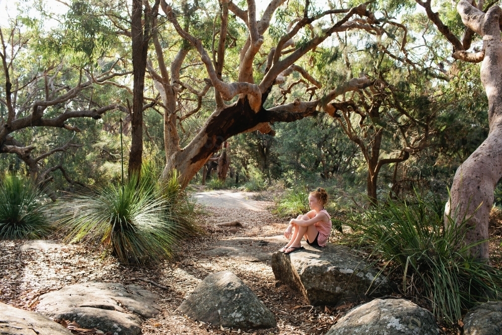 Girl sitting on a rock among trees - Australian Stock Image