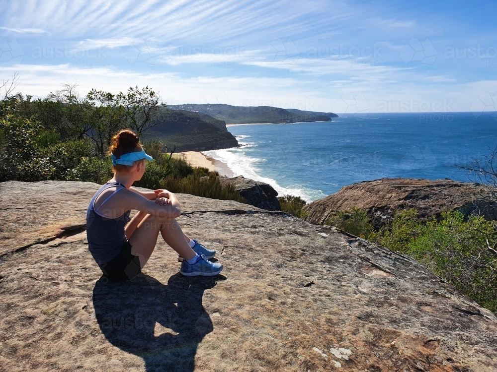 Girl sitting on a rock looking at the view of a beach - Australian Stock Image