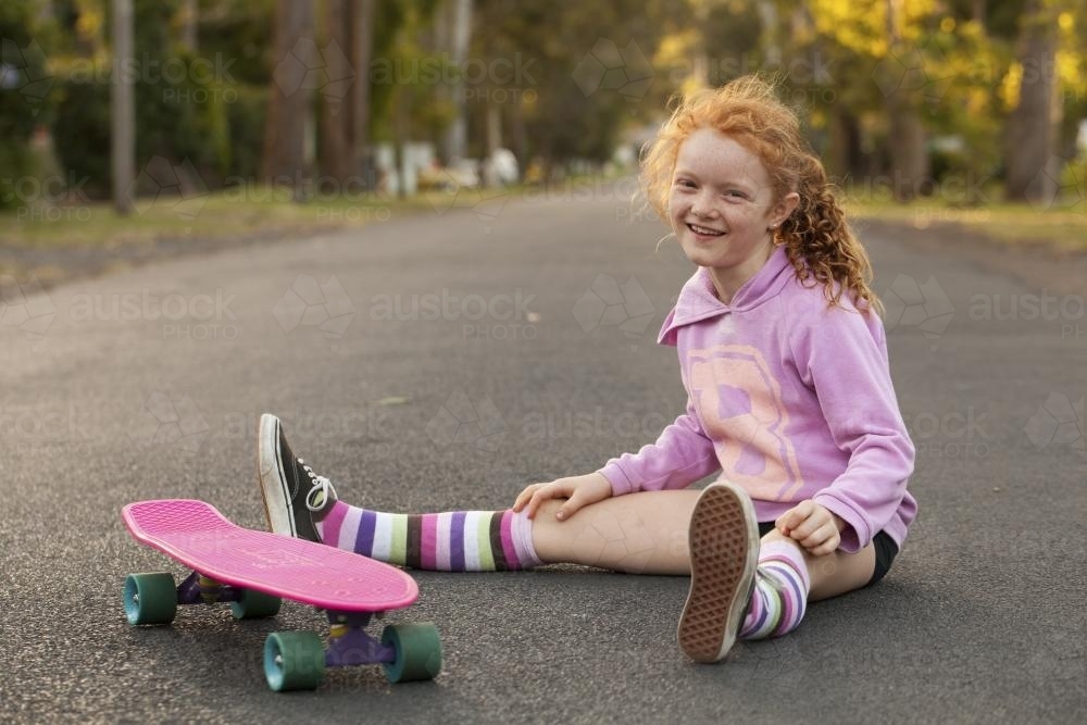 Girl sitting on a the street with a skateboard - Australian Stock Image
