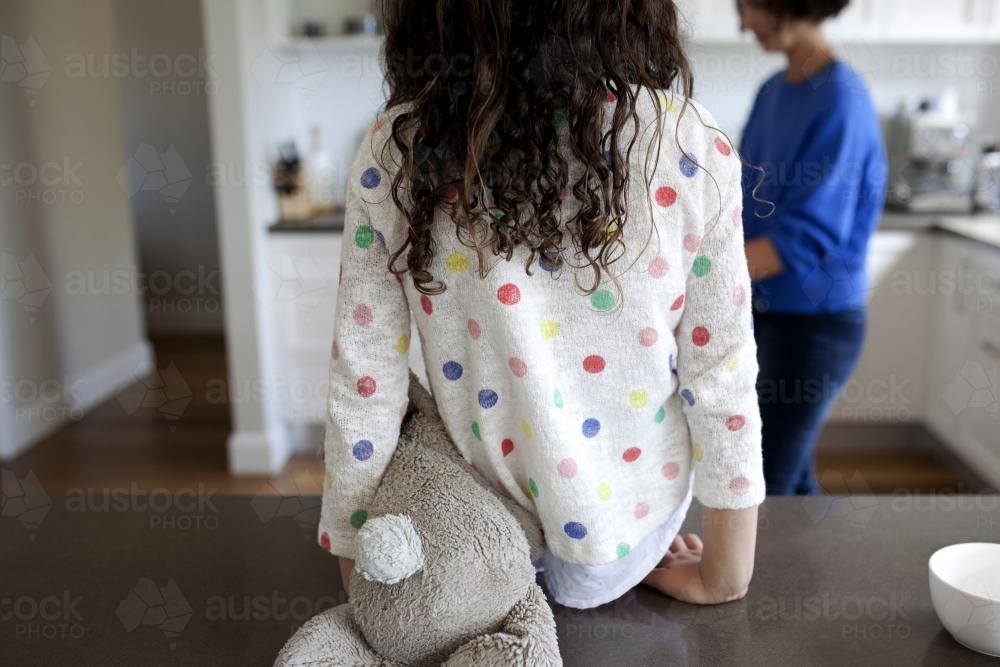 Girl sitting on kitchen bench top with soft toy - Australian Stock Image