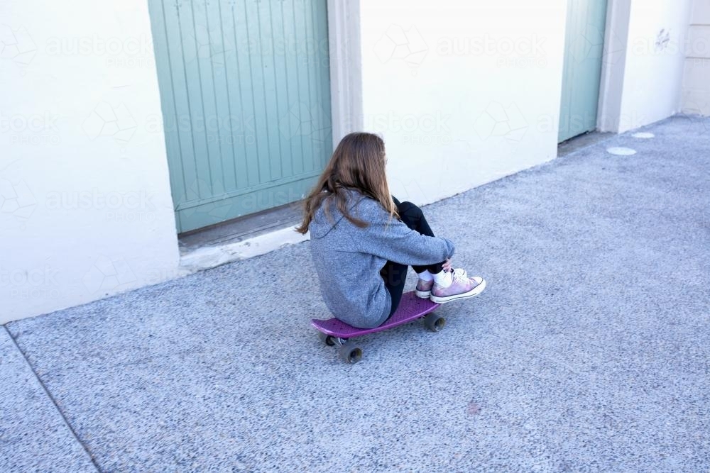 Girl sitting on skate board skating down street - Australian Stock Image