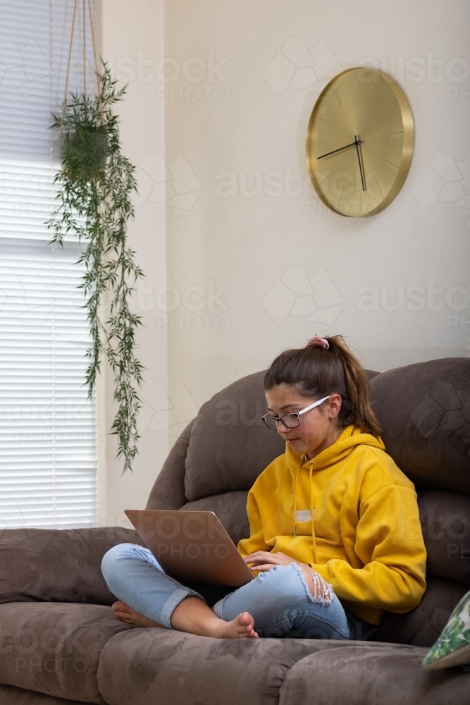 Girl sitting on sofa with laptop on crossed legs - Australian Stock Image