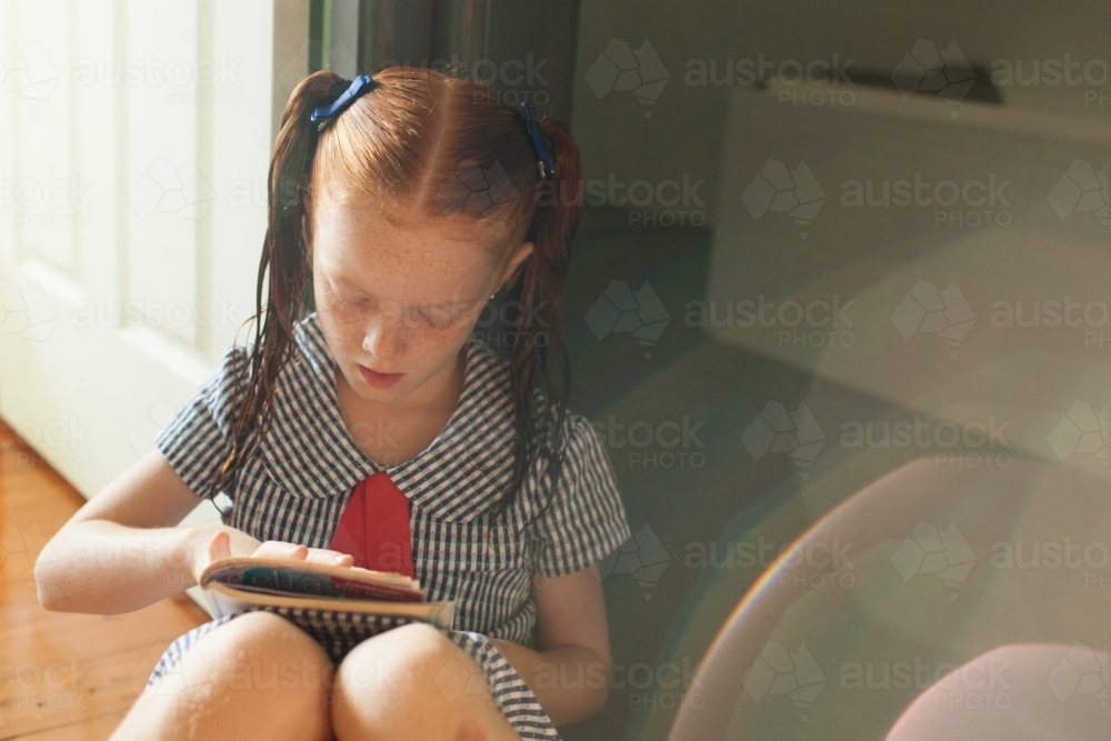Girl sitting on the floor reading a book - Australian Stock Image