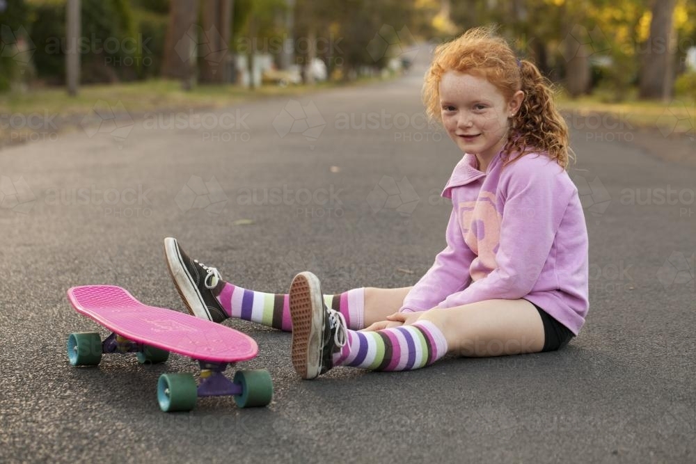 Girl sitting with a skateboard in the street - Australian Stock Image
