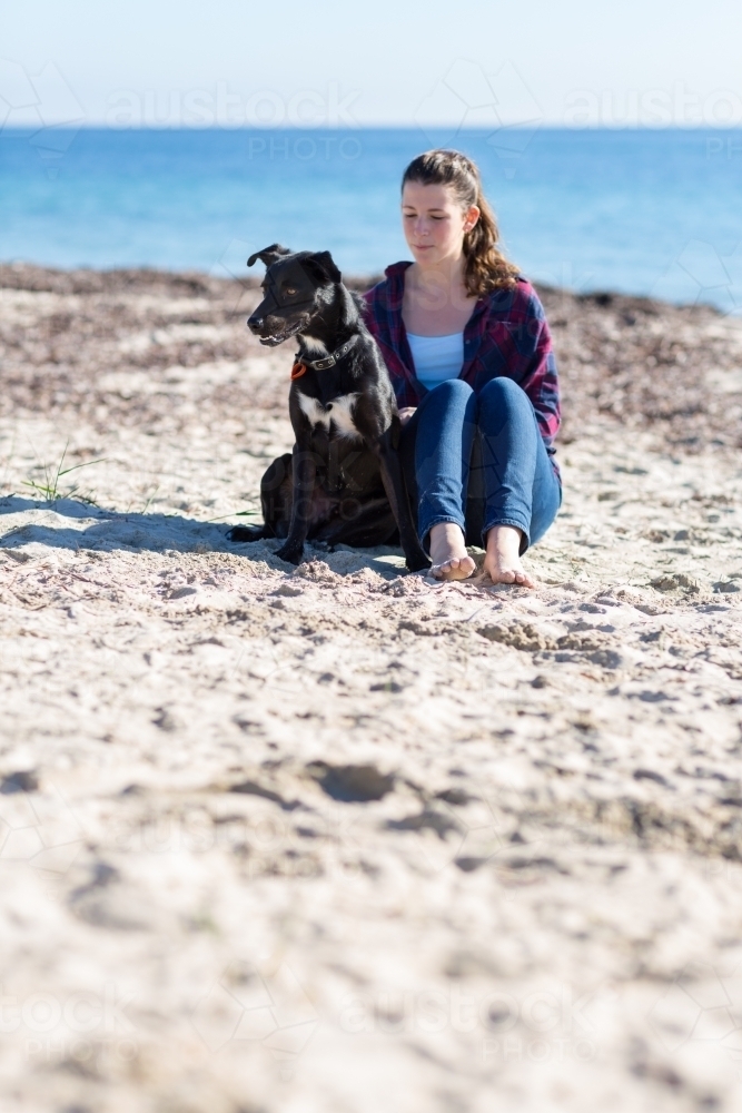 Girl sitting with dog on the beach - Australian Stock Image