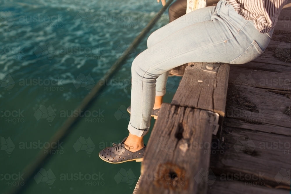 Girl sitting with legs dangling over a jetty - Australian Stock Image