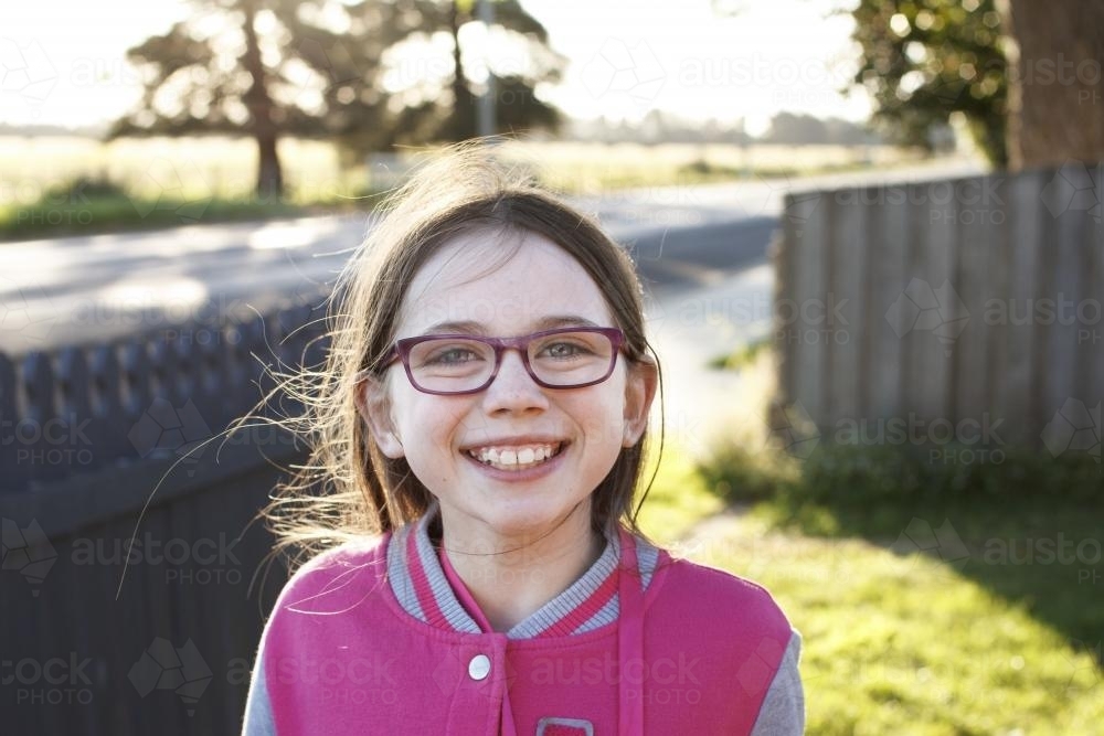 Girl smiling in the late afternoon sun in front yard of home - Australian Stock Image