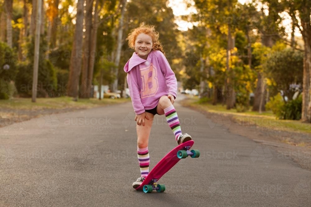 Girl smiling on a skateboard in the street - Australian Stock Image