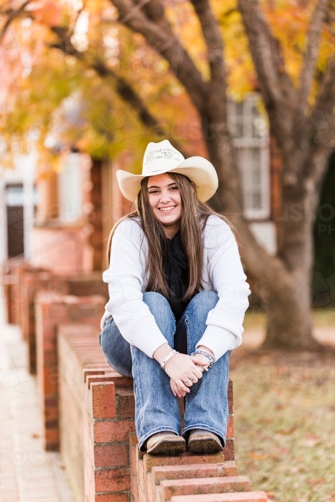 Girl smiling sitting on brick wall - Australian Stock Image