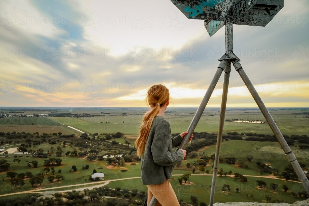 Girl standing at the summit of Pyramid Hill, Victoria looking at view of farmland below - Australian Stock Image