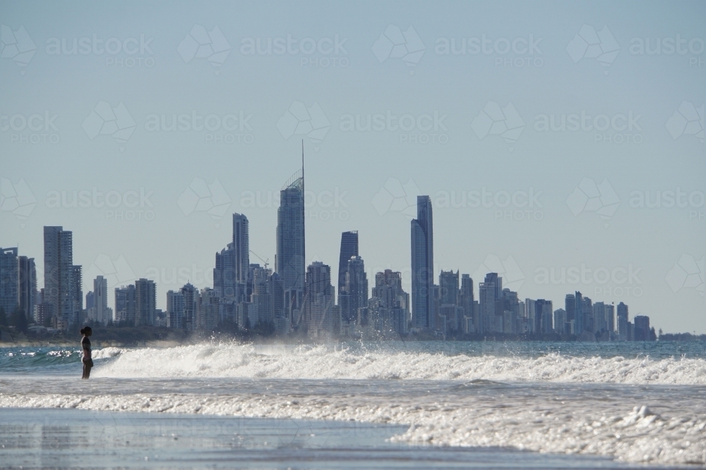 Girl standing in surf with Surfers Paradise in background - Australian Stock Image