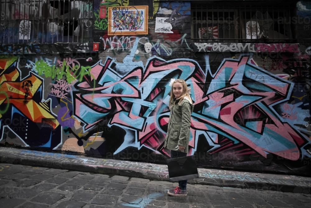 Girl standing in the street in front of graffiti with shopping - Australian Stock Image