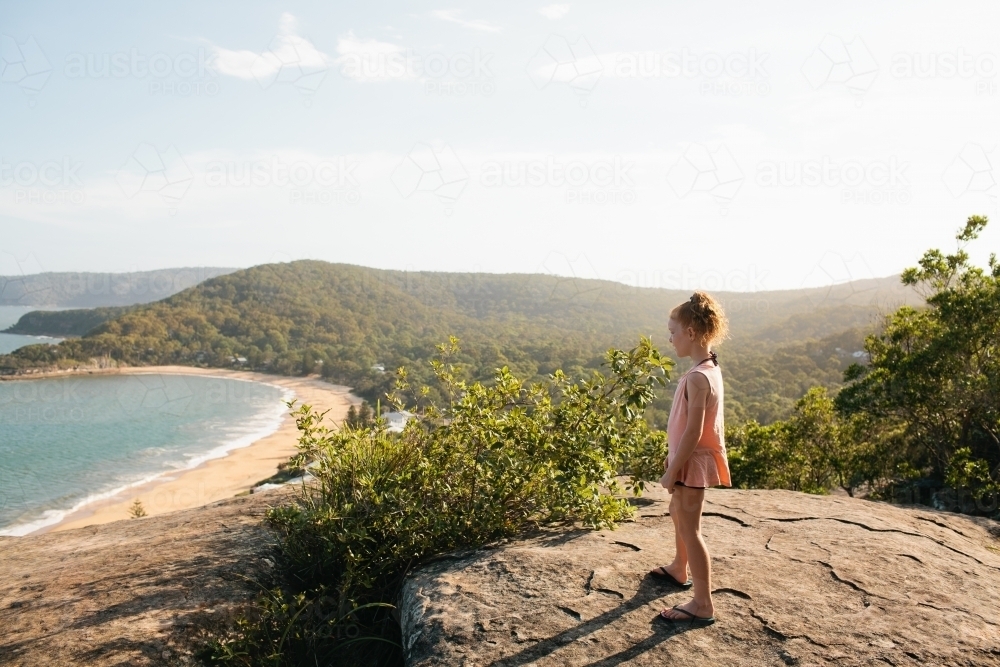 Girl standing on a rock looking at the view over a beach - Australian Stock Image