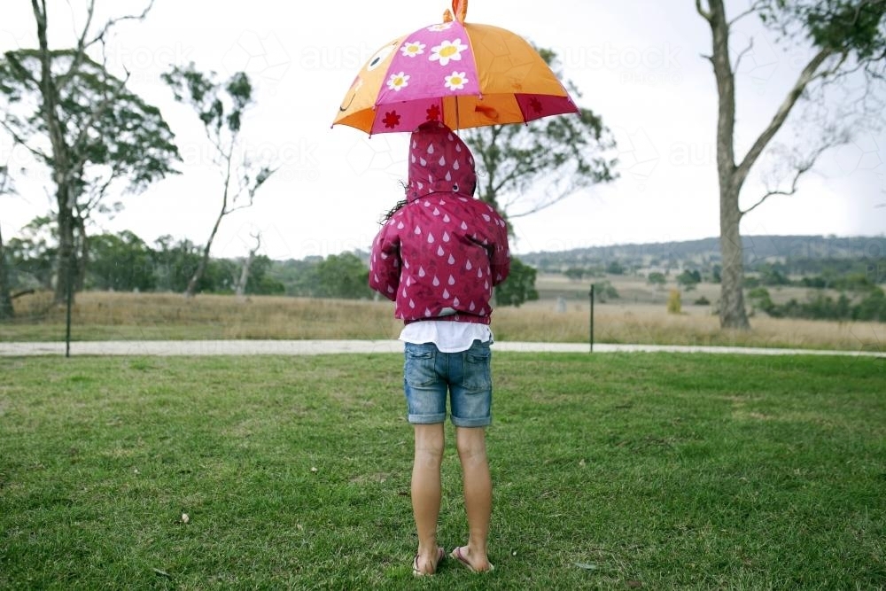 Girl standing outside in the rain with umbrella and raincoat - Australian Stock Image