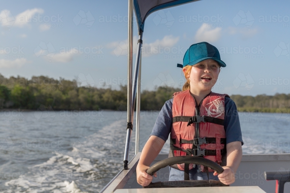 Girl steering a boat wearing a life jacket - Australian Stock Image