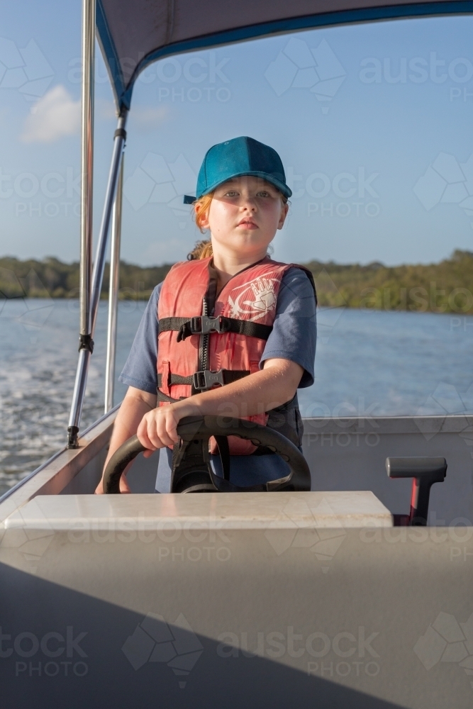 Girl steering a boat wearing a life jacket - Australian Stock Image