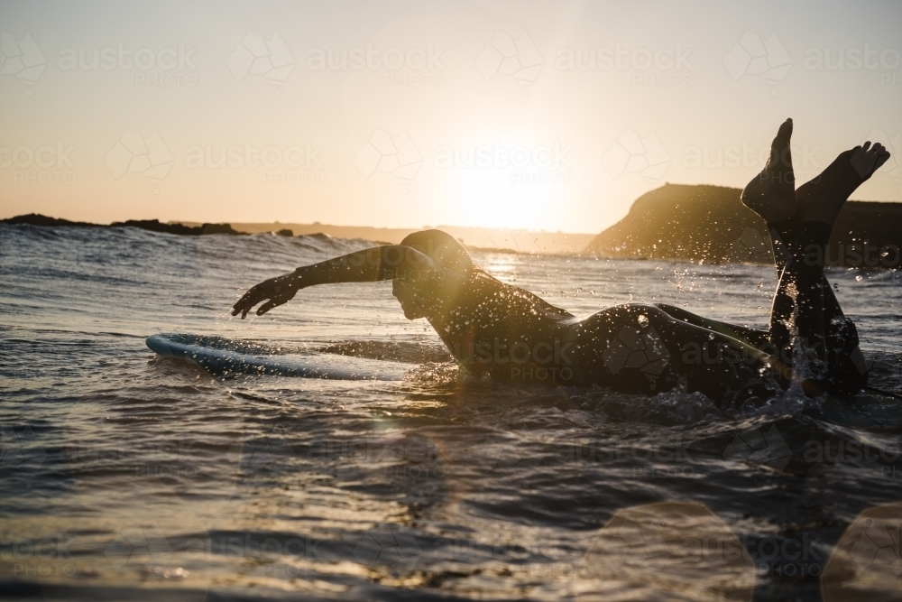 Girl surfing in the ocean on a longboard during sunset - Australian Stock Image