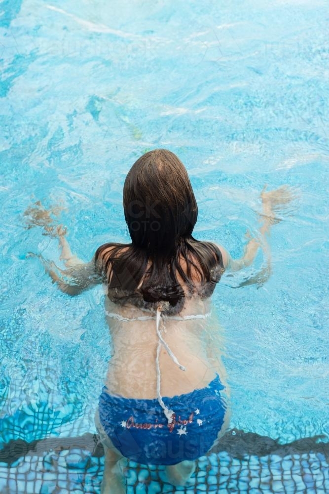 girl swimming in pool, from behind - Australian Stock Image