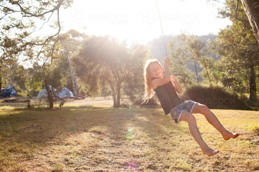 Girl swinging on a rope swing at a campsite - Australian Stock Image