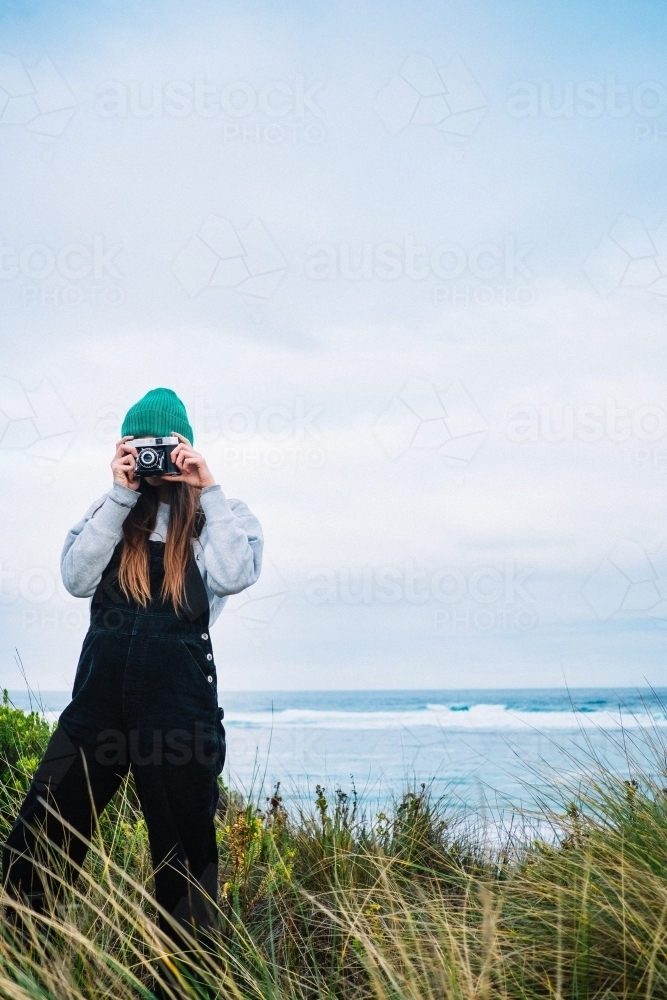 Girl taking photo with old school film camera at the beach - Australian Stock Image