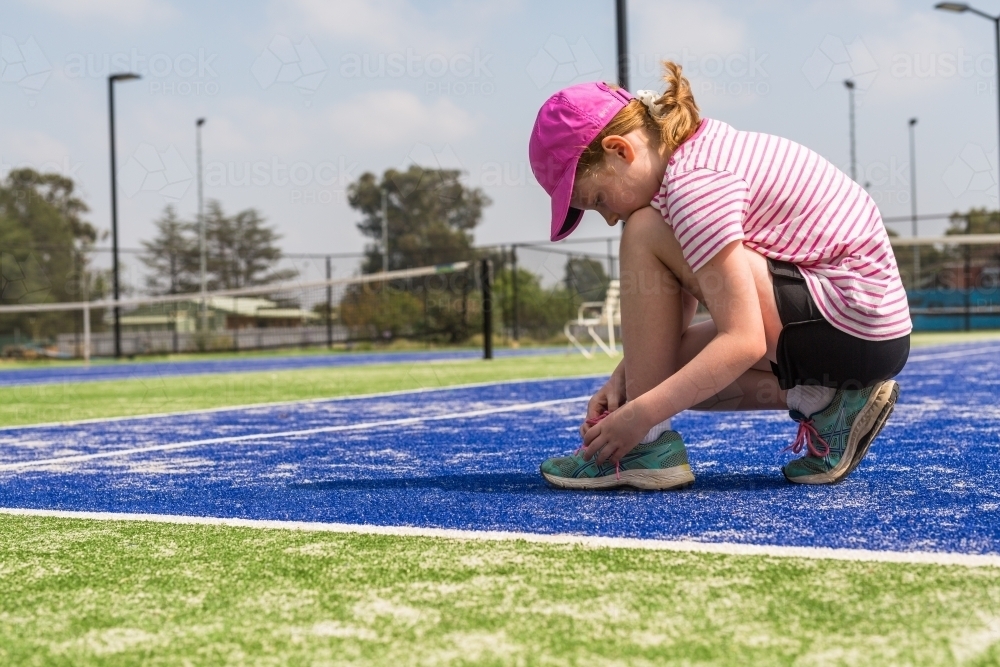 Girl tying her shoelaces on a blue tennis court - Australian Stock Image
