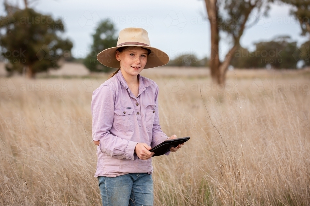 Girl using an ipad in a farm paddock - Australian Stock Image