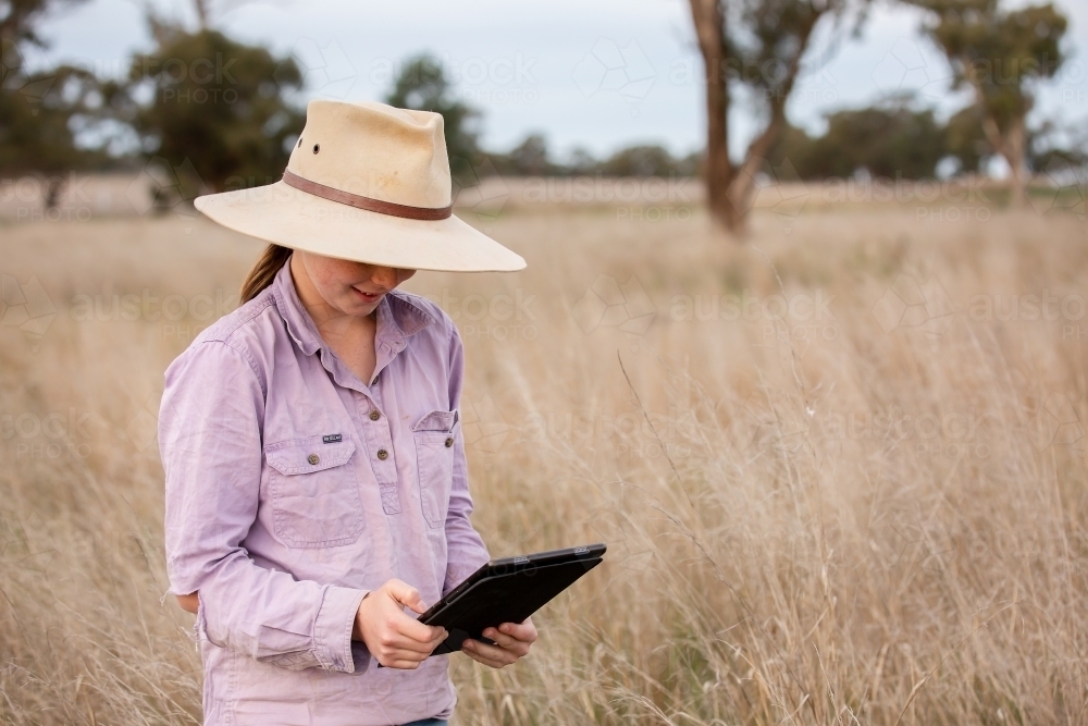 Girl using an ipad in the paddock on a farm - Australian Stock Image