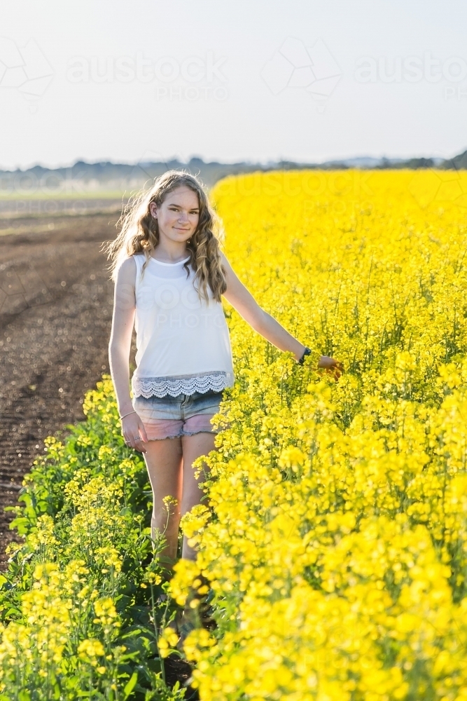 Girl walking along canola crop touching flowers on farm - Australian Stock Image