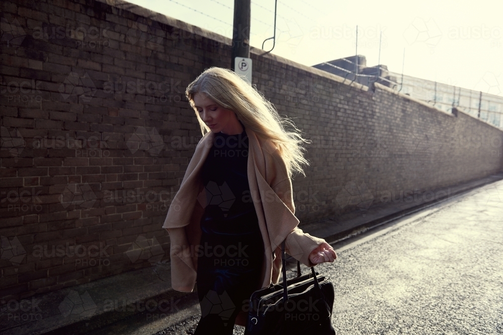 Girl walking down street alley backlit by sun next to brick wall - Australian Stock Image