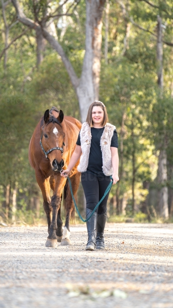 Girl walking horse toward camera smiling - Australian Stock Image