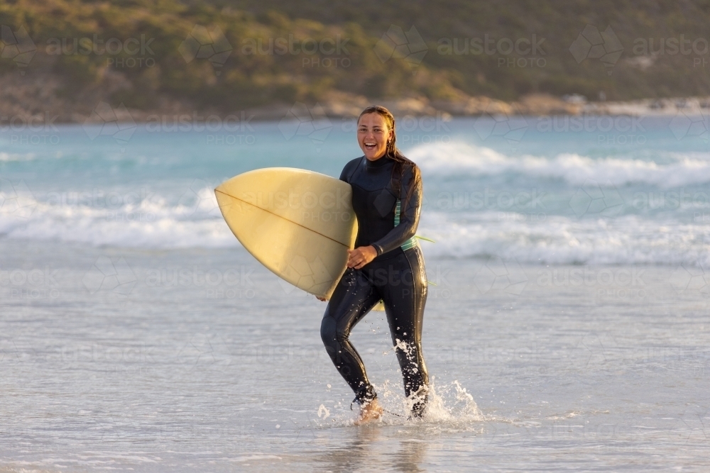 girl walking out of the water carrying surfboard on beach - Australian Stock Image