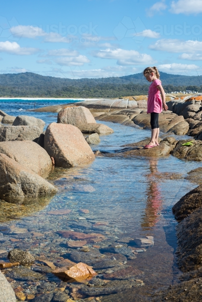 Girl walking over boulder rocks and rockpools at beach - Australian Stock Image
