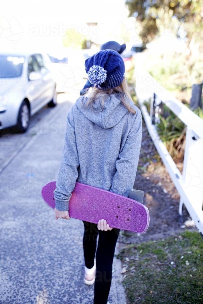 Girl walking up path holding skateboard behind her back - Australian Stock Image
